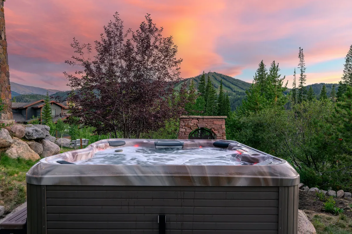 An exterior view of a custom hot tub set on a patio, with sweeping mountain views and a captivating sunset sky. The hot tub appears inviting and luxurious, positioned perfectly for soaking while admiring the natural scenery.