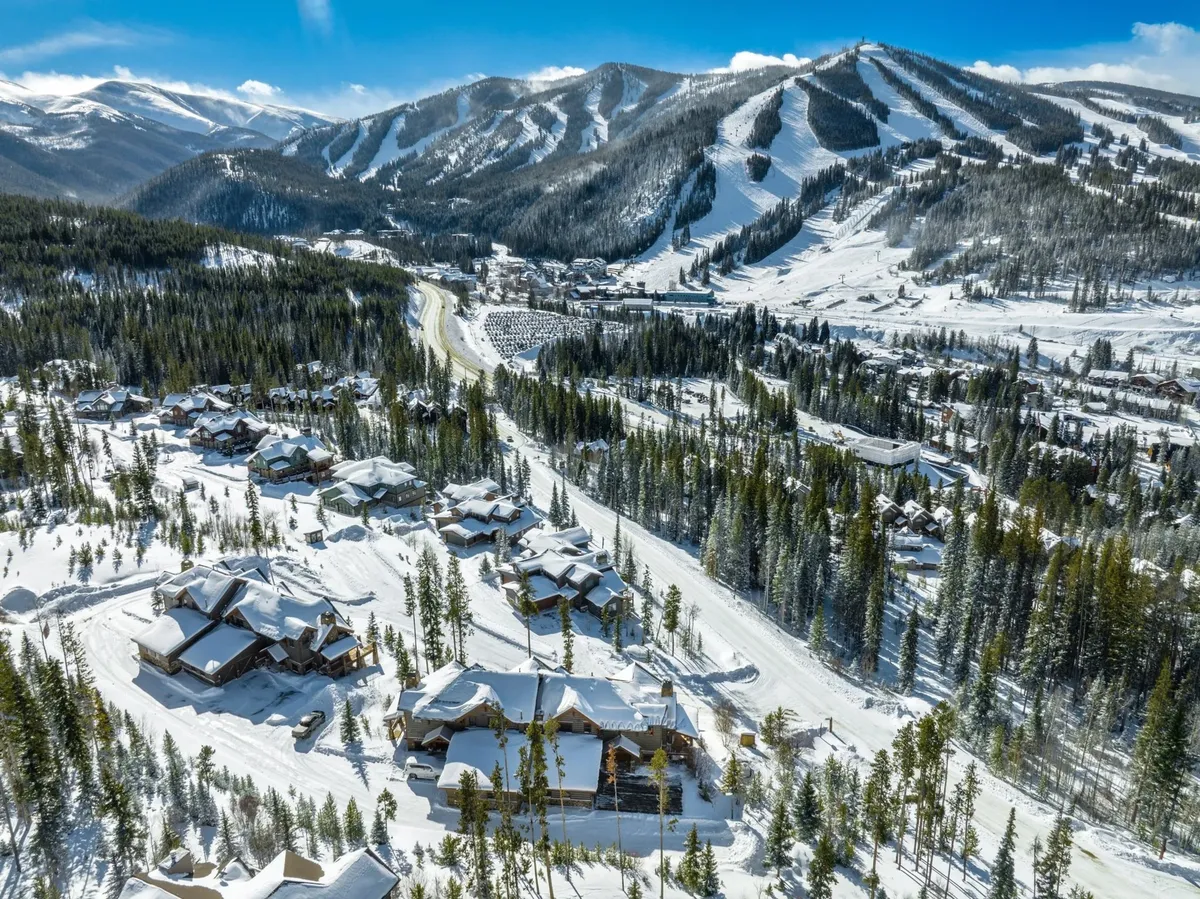 A sweeping view of snow-covered mountains, rustic wooden chalets nestled among pine trees, and winding roads hinting at adventures in every direction. The image encapsulates winter sports activities like skiing and snowboarding while suggesting scenic hiking and biking routes for warmer seasons.