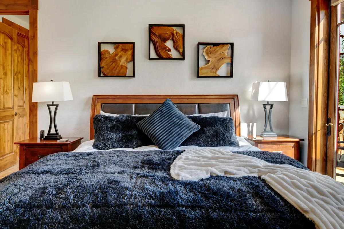 A tranquil bedroom featuring plush bedding, decorative pillows, nightstands with lamps, and tasteful wall art. Sunlight streams in, emphasizing the serene atmosphere and inviting guests to relax.
