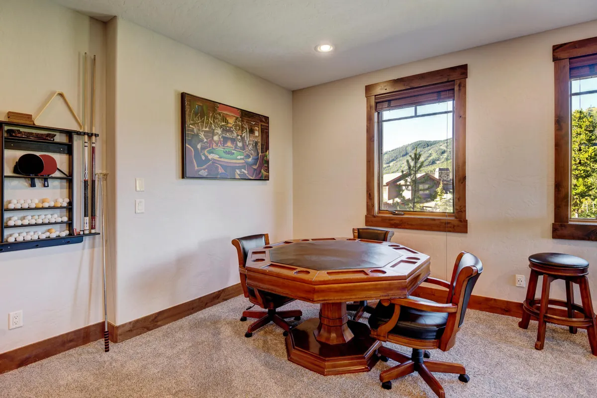 A cozy, light-filled space featuring an octagonal table designed for board games or cards, a pool cue rack for billiards enthusiasts, and large windows framing scenic views. The ambiance is warm and friendly, perfect for group games or enjoying downtime together.