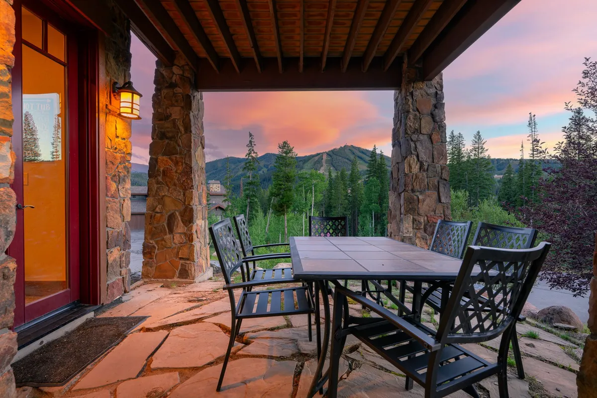 An outdoor dining table set beneath stone pillars, framed by expansive mountain views and a vibrant sunset sky. The ambiance suggests al fresco meals, social gatherings, and evenings spent stargazing in every season.