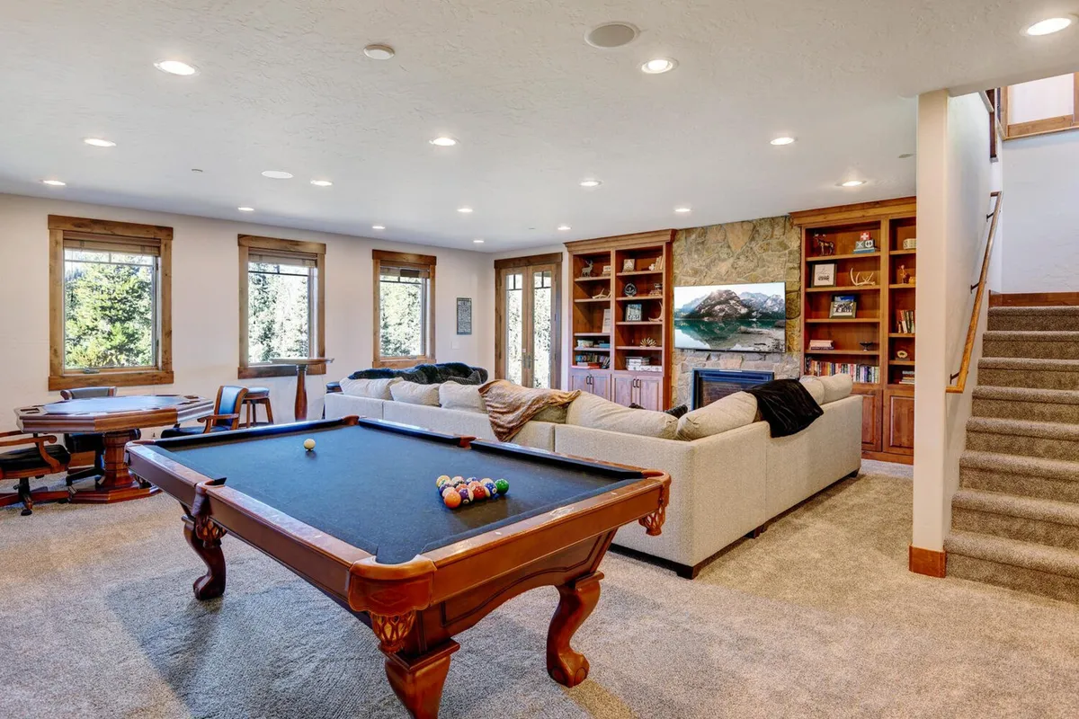 This image features a spacious game room with a pool table, comfortable sofa for lounging, wall-to-wall bookshelves, and large windows letting in natural light. The setup encourages friendly competition, relaxation, and social gathering, with the sofa positioned perfectly for watching TV or enjoying a movie night.